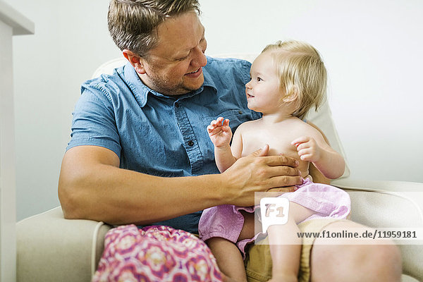 Vater mit kleinem Mädchen (12-17 Monate) im Wohnzimmer sitzend
