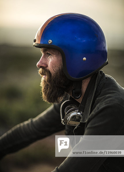 Profile of bearded man wearing blue open face crash helmet  goggles round his neck.