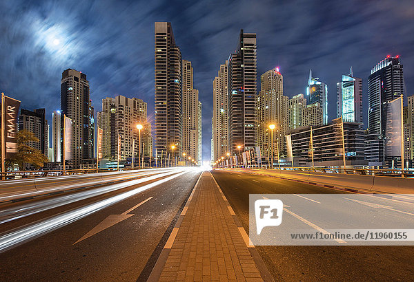 Stadtlandschaft mit beleuchteten Wolkenkratzern in Dubai  Vereinigte Arabische Emirate in der Abenddämmerung  im Vordergrund die Autobahn.