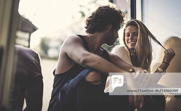 Ein Mann mit braunen Haaren in zerrissenen Jeans und eine Frau mit langen blonden Haaren sitzen im Freien  schauen sich an und lächeln.