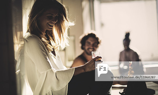 Side view of woman with long blond hair sitting indoors  holding beer glass  two men in background.