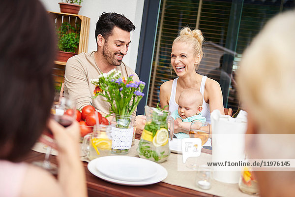 Couple with baby daughter at family lunch on patio table