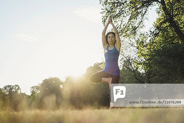 Mature woman in park  balancing on one leg  in yoga position  low angle view