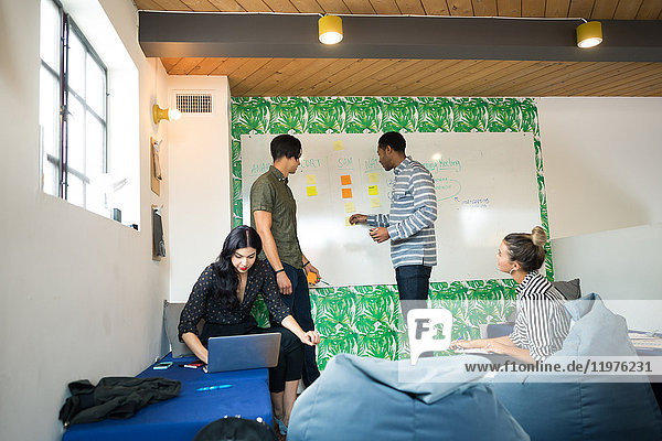 Junge Geschäftsleute nutzen Laptop und Whiteboard im kreativen Sitzungsraum