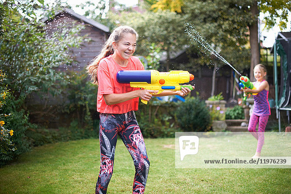Teenager-Mädchen und ihre Schwester haben eine Wasserpistolenschlacht im Garten