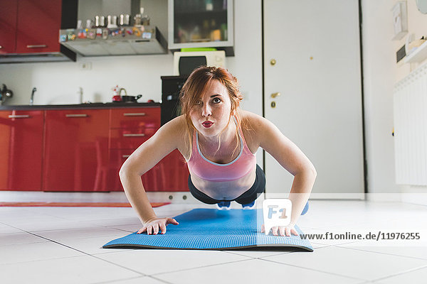 Portrait of young woman doing push ups on kitchen floor