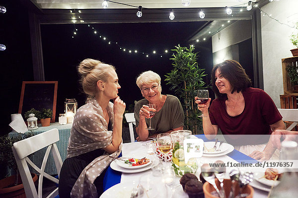 Drei Frauen sitzen am Esstisch und trinken aus Weingläsern