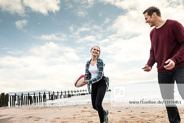 Vater und Tochter spielen Rugby am Strand