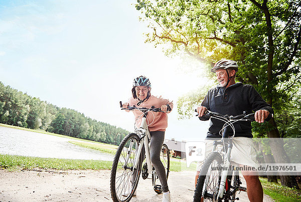 Mature couple cycling beside lake  laughing  low angle view