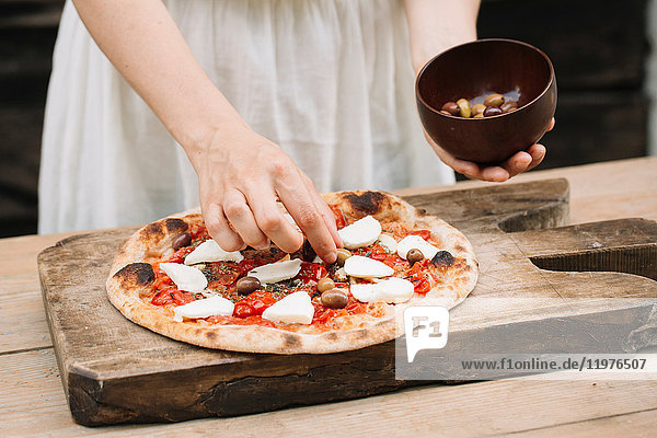 Frau legt Oliven auf hausgemachte Pizza  Mittelteil