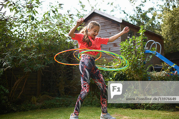 Teenager-Mädchen beim Hula-Hoop-Reifen mit vier Plastikreifen im Garten