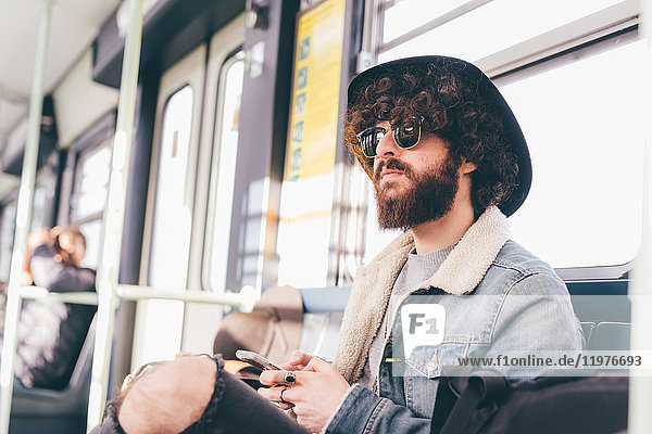 Young man sitting on subway train  using smartphone