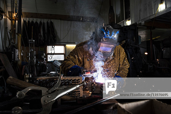 Schmied in Schweißmaske schweißt Metall in Werkstatt
