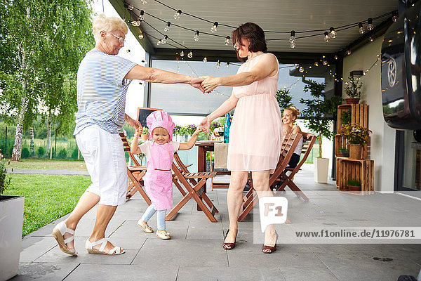 Ältere und reifere Frauen tanzen mit einem weiblichen Kleinkind beim Familienessen auf der Terrasse
