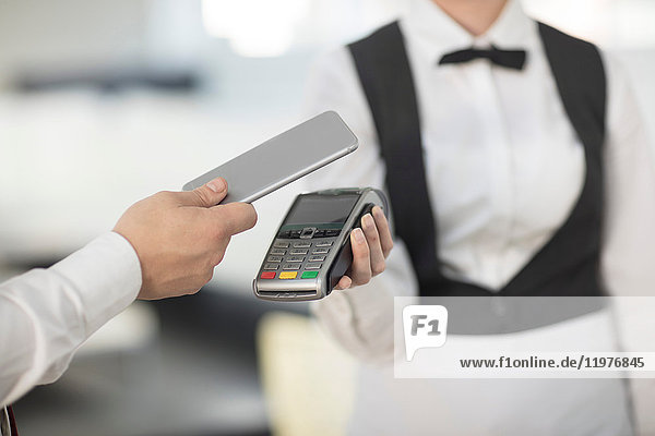 Kellnerin hält Zahlungsautomat in Richtung Kunde  Kunde bezahlt kontaktlos