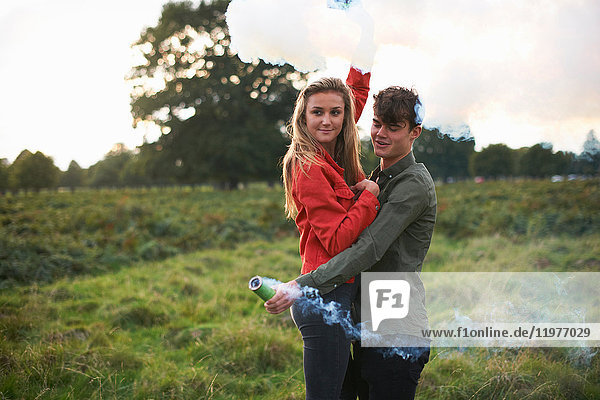 Young couple letting off smoke flares in field