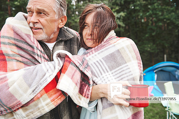Mature couple standing beside tent  wrapped in blanket