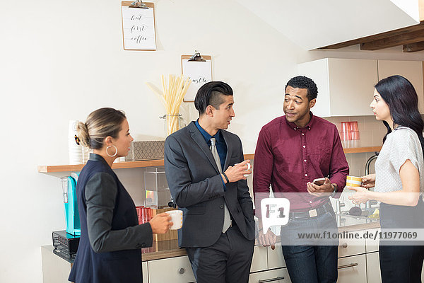 Businesswomen and men having informal meeting in office kitchen