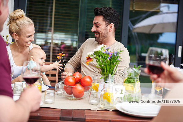 Couple with baby daughter at family lunch on patio table