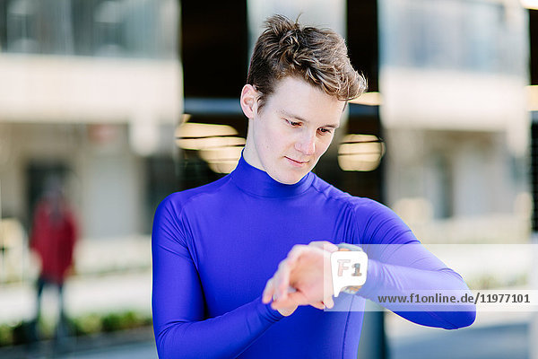 Young male runner looking at smartwatch on city sidewalk