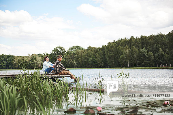Mature couple relaxing on jetty beside lake