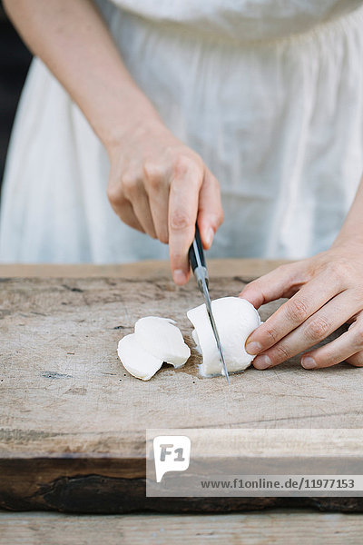 Woman slicing mozzarella on chopping board  mid section