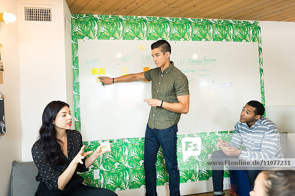 Junger Geschäftsmann zeigt auf Whiteboard in kreativem Besprechungsraum