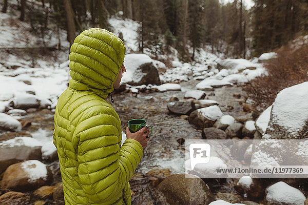 Junger männlicher Wanderer mit Kaffee am verschneiten Waldfluss  Sequoia-Nationalpark  Kalifornien  USA