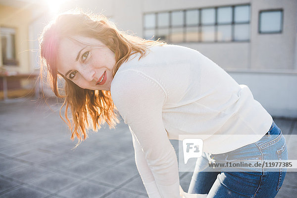 Portrait of beautiful young woman bending forward on sunlit roof terrace
