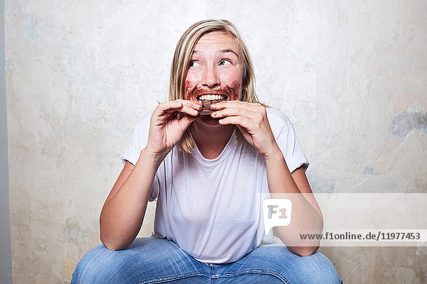 Porträt einer Frau  die eine Tafel Schokolade isst  Schokolade um den Mund