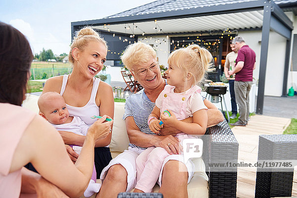 Frauen der dritten Generation mit Kindern auf dem Schoß beim Familienessen auf der Terrasse