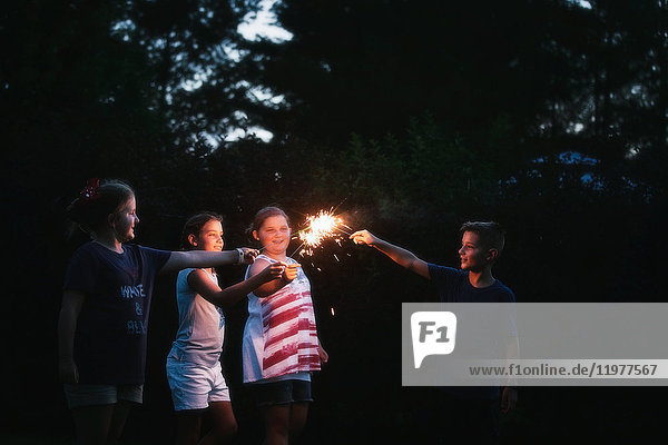 Junge und drei Mädchen zünden am Unabhängigkeitstag nachts gemeinsam Wunderkerzen an  USA
