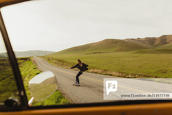 Autofensteransicht eines jungen männlichen Skateboardfahrers beim Skateboarden entlang einer Landstraße,  Exeter,  Kalifornien,  USA