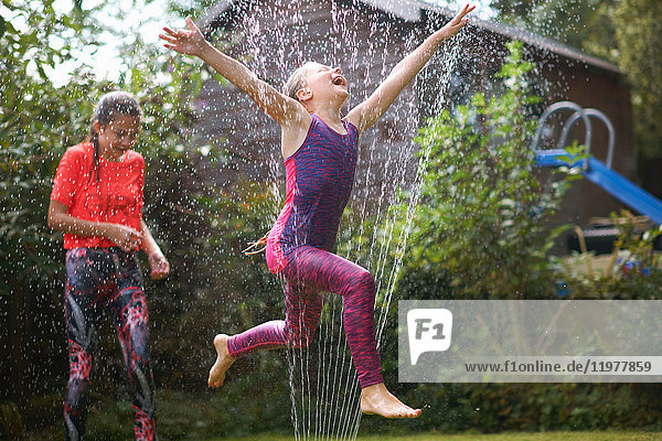 Girls jumping over garden sprinkler