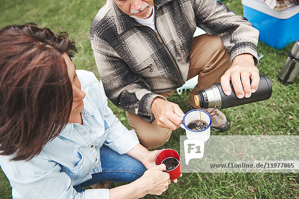 Mature couple crouching on grass  man pouring hot drink from drinks flask  elevated view