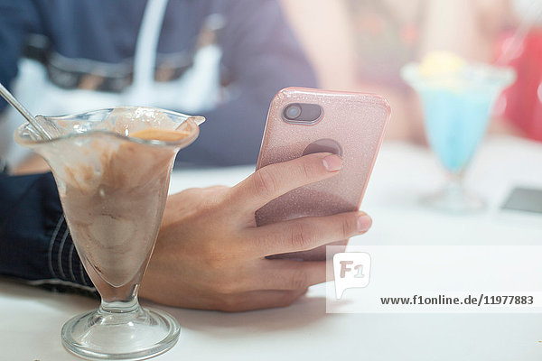 Young man sitting in diner  using smartphone  mid section  close-up