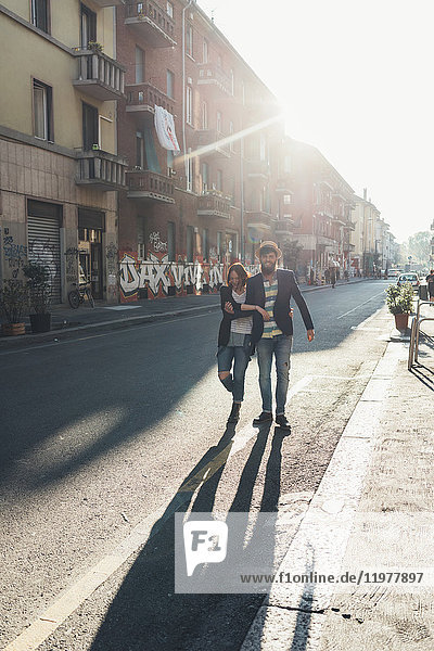 Glückliches Paar schlendert die sonnenbeschienene Straße entlang
