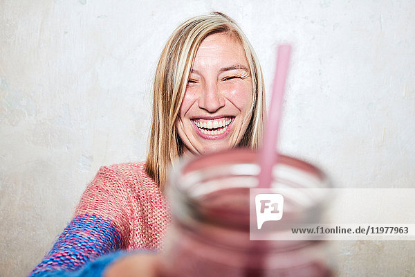 Porträt einer Frau  die ein Getränk in die Kamera hält und lacht