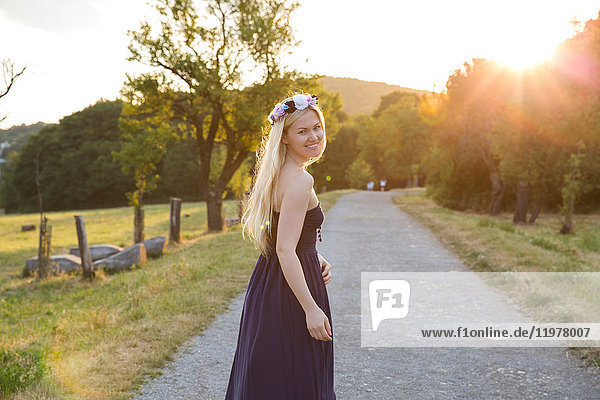 Woman on rural road wearing strapless dress looking over shoulder at camera smiling