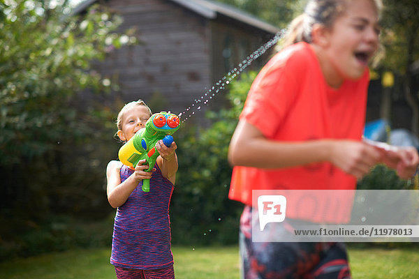 Junge bespritzt seine jugendlichen Schwestern mit Wasserpistole im Garten