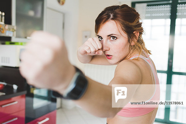 Young woman doing boxing training in kitchen