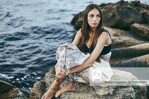Junge Frau sitzt auf einem Küstenfelsen und schaut über ihre Schulter  Odessa  Ukraine