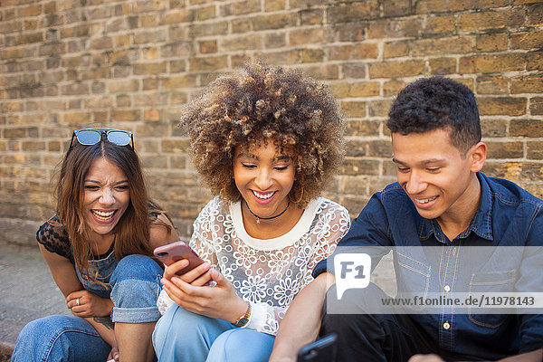 Drei Freunde sitzen auf der Straße und schauen auf ein Smartphone