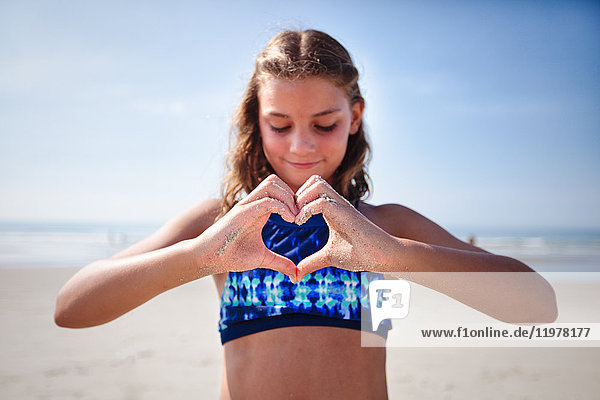 Mädchen macht Herzform mit Händen am Strand