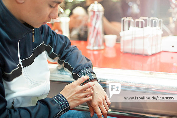 Young man sitting in diner  using smartwatch  mid section