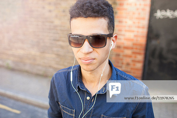 Porträt eines jungen Mannes im Freien  der eine Sonnenbrille und Kopfhörer trägt