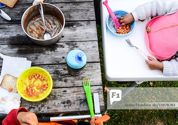 Cropped overhead view of two toddlers eating baked beans on camping site
