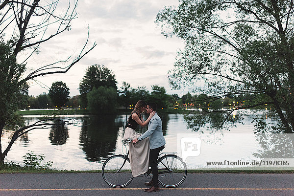Romantisches junges Paar auf dem Fahrrad am See in der Abenddämmerung von Angesicht zu Angesicht