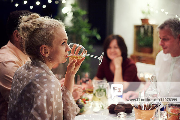 Group of people sitting at table  enjoying meal  young woman drinking from wine glass