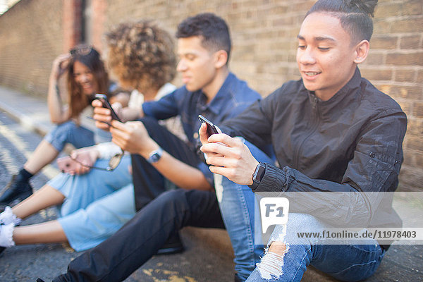 Vier Freunde sitzen auf der Straße und schauen auf Smartphones